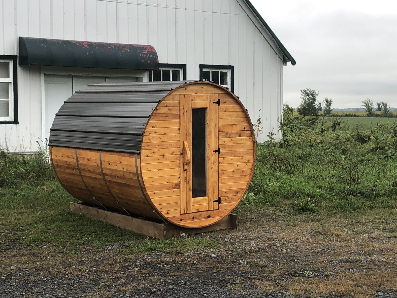 A small wooden barrel sauna on a lawn beside a house