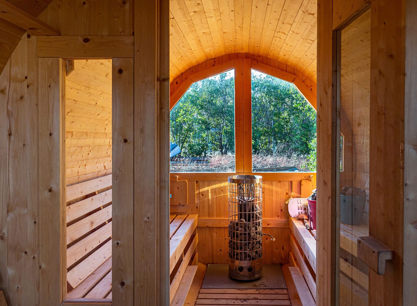 Inside a barrel sauna: wooden benches, a heater and a round window